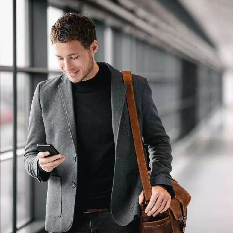 Mann mit Smartphone und Tasche unterwegs am Flughafen